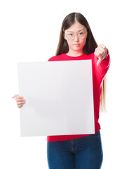 Young Chinese woman over isolated background holding blank banner with angry face, negative sign showing dislike with thumbs down, rejection concept