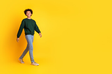 Full body portrait of nice young man walk empty space ad wear sweater isolated on yellow color background
