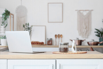 Modern laptop, statuette and jar with coffee beans on table in dining room