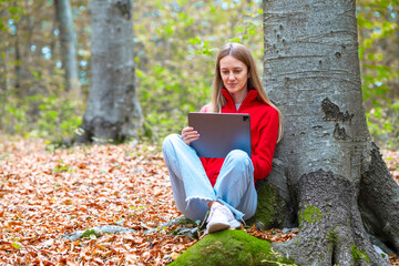 A girl on a walk in the forest in a red warm fleece jacket holds a work tablet in her hands....