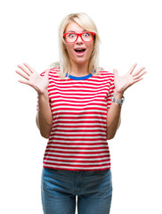 Young beautiful blonde woman wearing glasses over isolated background celebrating crazy and amazed for success with arms raised and open eyes screaming excited. Winner concept