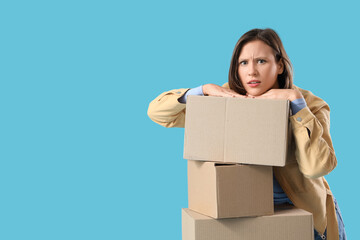Beautiful young worried woman with many parcels on blue background