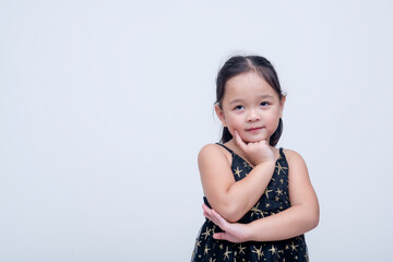 A cute little asian girl posing pensively. Wearing a starry black dress. Isolated on a white...