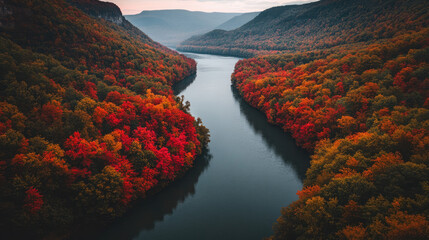 The calm river meanders gracefully through a valley blanketed in autumn hues. The vivid red and orange leaves of the trees create a stunning contrast against the reflective water.