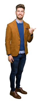 Young handsome business man smiling with happy face looking and pointing to the side with thumb up.