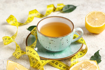 Cup of tea for weight loss, lemons and measuring tape on white grunge table, closeup