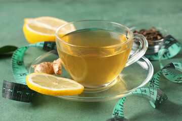 Cup of tea for weight loss, lemons and measuring tape on green table, closeup