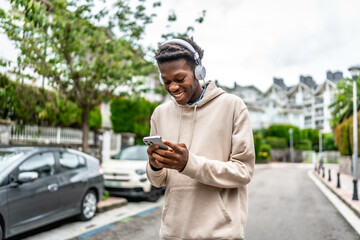 African young student using phone and listening to music outdoors