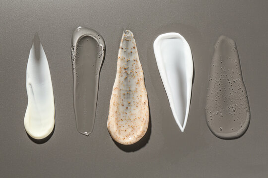 Smears of different cosmetic products on grey background, flat lay