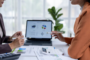 Two businesswomen analyzing financial graphs on laptop using pens and calculator