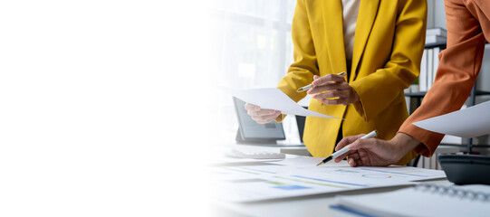 Two businesswomen discussing financial charts and documents at office desk
