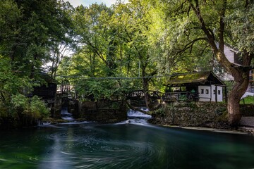 Serene riverside scene with waterfall and bridges in a lush village.