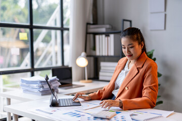 Businesswoman analyzing financial charts and using laptop at office desk