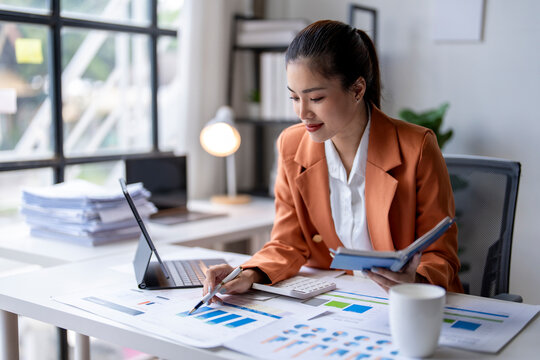 Young asian businesswoman analyzing financial chart using digital tablet and calculator in office - Powered by Adobe
