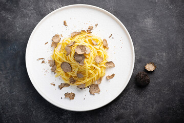 Black truffle pasta Tajarin. Black rustic table, magical autumn light, front view. Autumn gourmet cuisine of Piedmont, Northern Italy, Spain and France