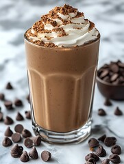 Chocolate smoothie in a clear glass with cocoa powder, chocolate chips, and a dollop of whipped cream on the side