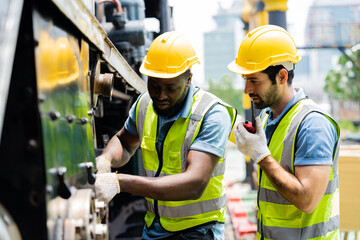 Two men in yellow safety vests are working on a train. One of them is holding a tool
