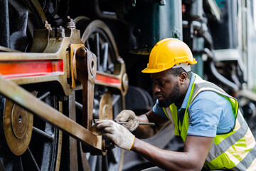 A man in a yellow helmet is working on a train engine. He is wearing a safety vest and gloves