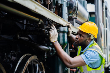 A man in a yellow helmet is working on a train engine