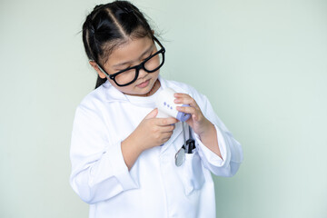 Cute girl in a medical mask plays a doctor and measures the temperature with a non-contact thermometer.