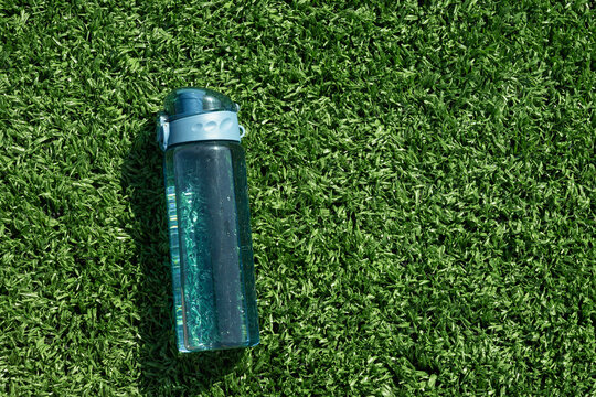 Refreshing blue bottle of water in sunny day on outdoor soccer sports ground with artificial grass covering. Concept water balance for workout. View from above. Copy space. - Powered by Adobe