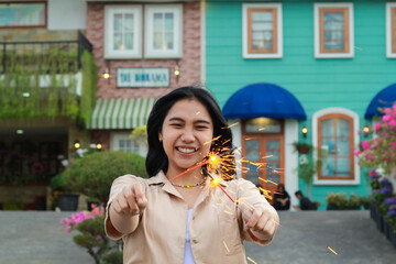 Fototapeta premium happy young asian woman holding sparkler celebrating new year eve in vintage house yard, outdoor garden