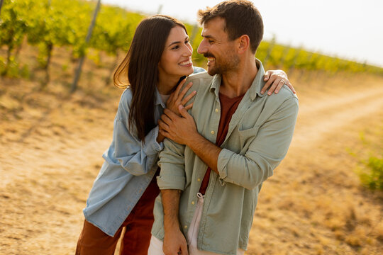 A joyful couple laughing together in a sunlit vineyard during a warm afternoon, surrounded by lush grapevines and a rustic path
