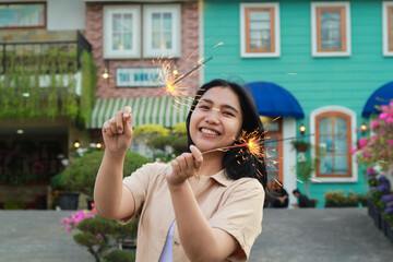 portrait of beautiful happy young asian woman holding sparklers fireworks to celebrate new year eve with garden party standing in outdoor vintage house yard