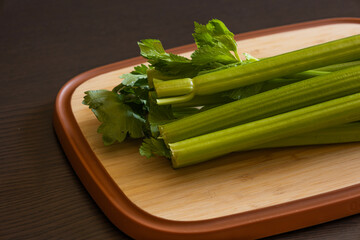 Bunch of Celery on Wooden Board Close-Up on Dark Background