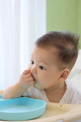 The baby is sitting in a high chair and learning to eat green vegetables