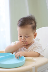 The baby is sitting in a high chair and learning to eat green vegetables