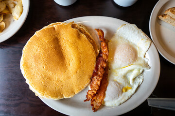 A stack of fluffy American pancakes with two fried eggs and two strips of bacon.