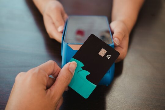 A hand making a contactless payment using a debit or credit card on an electronic data capture device or EDC - Powered by Adobe