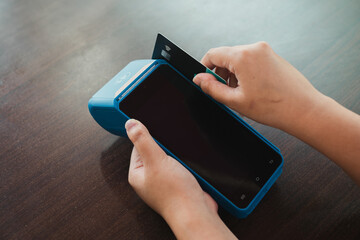A hand making a payment by swiping a debit or credit card on an electronic data capture device or...