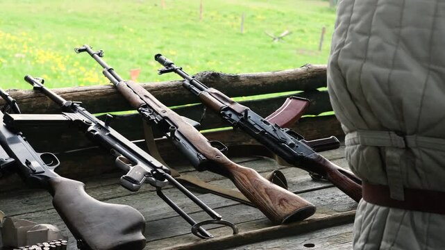 Soldier in military uniform is taking a submachine gun from a table on a shooting range