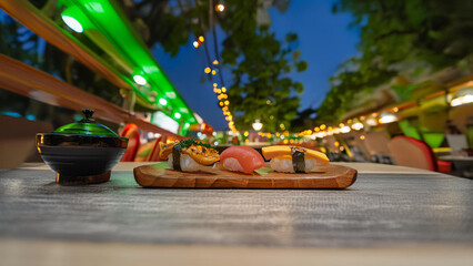 Vibrant Nighttime Sushi Platter Under Festival Lights. Close-up of a sushi selection on a dark plate, set against a bokeh background of sparkling lights and green canopy. Vibrant, appetizing image per
