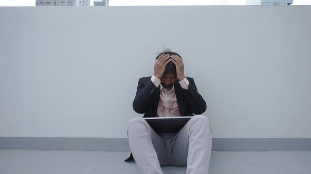 A businessman in formal attire sits on the ground with his head in his hands, conveying frustration or stress. The isolated setting highlights personal or professional challenges.