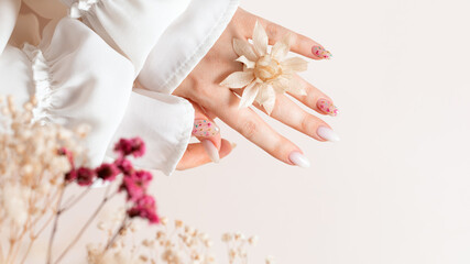 Spring manicure of woman hands with white gel polish and dried flower design. Female hands hold...
