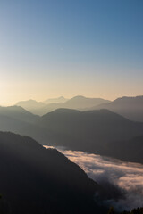Serene alpine landscape at dawn in Gailtal Alps, Carinthia, Austria, Europe. Silhouette of majestic hazy mountain ridges against morning sky. Valley covered in fog, clouds. Peaceful serene atmosphere