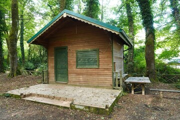 House made of vertical boards. The front door is closed, the window is closed with shutters, unfinished terrace. Near the house there is a table and a bench for lovers of simple rest.