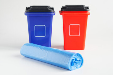 Rolled blue polyethylene garbage bags near two plastic waste bins or containers. White background....