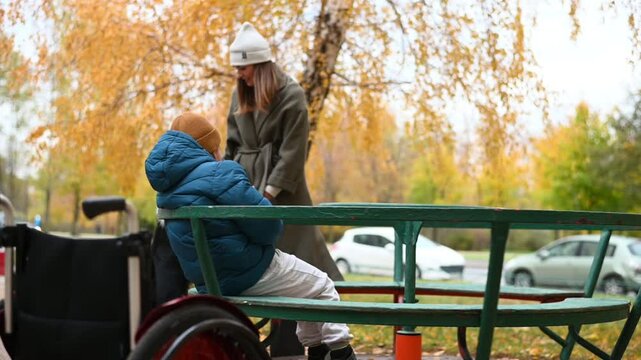 mother with disabled child in disabled Kremlin walk in autumn on the playground on the carousel. High quality FullHD footage