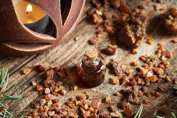 A transparent bottle of essential oil with myrrh resin and a candle