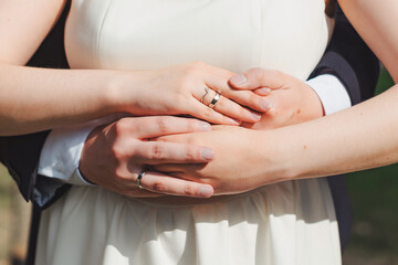 Couple embracing in a romantic moment outdoors during a sunny day, showcasing their wedding rings and love