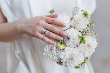 Bride holding a delicate bouquet of white and purple flowers on her wedding day in an outdoor setting