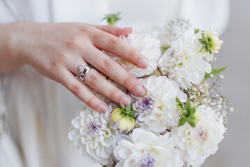 A hand gently rests on a bouquet of white dahlias arranged with delicate greenery in a soft, natural light