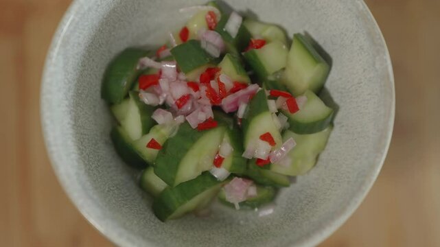 Une salade de pickles de concombre d'&eacute;chalottes d'&eacute;chalottes coup&eacute;s en petits morceaux dans un pot en c&eacute;ramique grise qui tourne vers la gauche sur un fond de planche &agrave; d&eacute;couper en bois