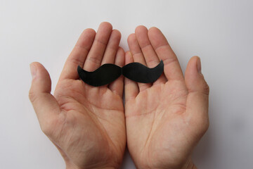 Male hands holding black paper moustache on white background. Movember, awareness about men's health, Father's Day promotions or for social media content about moustache culture