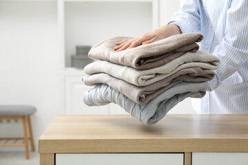 Woman with stack of clean clothes near wooden dresser indoors, closeup