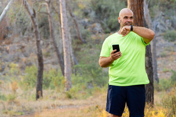 Naklejka premium Sporty man talking on the phone through smart watch, in the forest